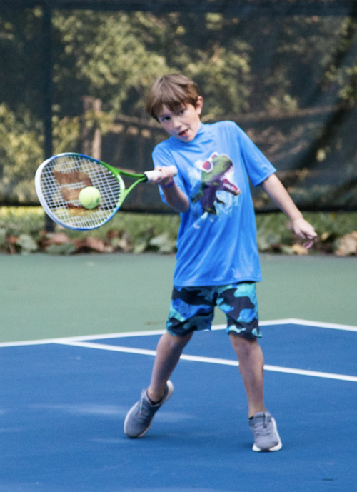 Photo of a boy in a blue shirt swinging a racket at a tennis ball at Tally Ho Potomac Tennis Club