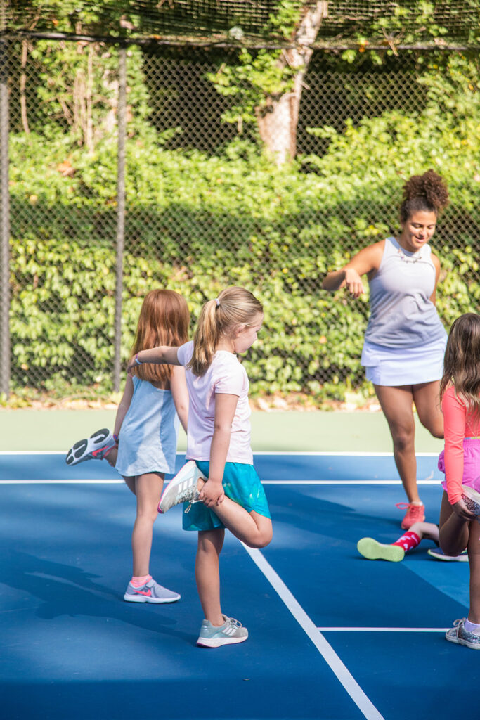 Photo of kids being led in a standing stretch at summer tennis camp