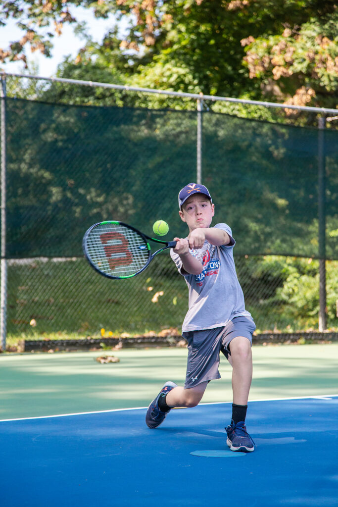 Photo of an active young player mid-swing, taking tennis lessons.