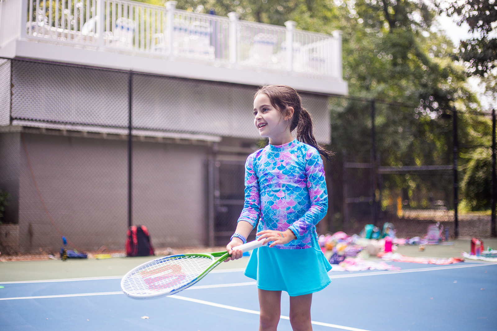 Photo of a smiling girl holding a tennis racket, taking junior tennis lessons at Old Georgetown Tennis Club